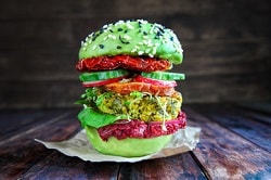 veganer Burger mit grünem Burgerbrötchen und schwarzen Sesam und weißen Sesam. Großer Burger mit getrockneter Tomate und weiterem Gemüse.
