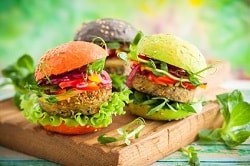 drei vegetarisch-vegane Burger mit viel Salat und farbigen Burgerbrötchen