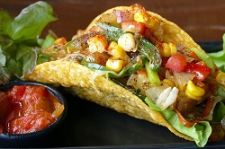 Ethno food_Auf dem Bild ist ein Taco zu sehen der mit viel gemüse gefällt ist. Daneben steht eine kleine Schüssek mit Salsa.