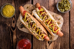 Hot Snacks_auf dem Bild sind zwei riesen hot dogs zu sehen, die von oben fotografiert wurden. beide liegen auf einem Brett und haben als topping eine Senf spur.