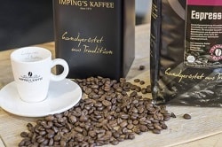 Auf dem Foto erkennt man eine Espresso-Tasse mit Untertasse und ausgestreuhte Kaffeebohnen rechts von der Tasse. Außerdem befinden sich jeweils rechts und dahinter eine Packung Espressobohnen auf dem Holztisch.