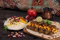 Ein typischens persisches Gericht, mit Reis, Gemüse und Brot sowie Fleischbälcchen in einem Warp drapiert mit Limette und Koriander.
