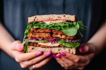 Frau mit Nagellack hält veganes Sandwich Fleischalternative Fleischersatz