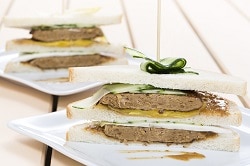 Drei Snadwich Brote mit jeweils drei Scheiben Toast, belegt mit einem Vegetarischen Quorn Burger Pattie, Gurke und einer gelben Snacksoße. Angferichtet auf eienm weißen Teller. Ein Sancwich liegt im Vordergrund, ein zweites etwas verschwommen im Hintergrund