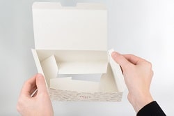 Rausch Verpackungen: zwei Hände die eine weiße rausch Verpackung in den Händen hält und diese gerade in der luft zusammenfaltet für den gebrauch.