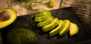 Durch die schwarze Farbe des Teller, kommt die grüne Außen- und gelbe Innenfarbe der Avocadostücke besonders zu Geltung. Die gefrorenen Avocado Slices sind mit der grünen Seite zum Zuschauer gewandt, angerichtet. Unten links sieht man noch eine ganz Avocado mit Schale und Kern.