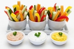 Auf dem Foto sind drei Behälter mit Gemüse Stäbchen aus Gurke, roter und gelber Paprika und Karotte zu sehen. Davor sind drei Schälchen mit Dip zu erkennen. Ganz Links ist ein hellrosaner Dip, in der Mitte ein weißer und ganz rechts ein gelber. Das Geschirr ist weiß und steht auch vor einem weißen Hintergrund.
