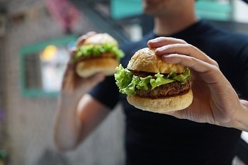 Vegane Burger gehalten von einem jungen Mann, welcher nur sekundär im Bild ist.