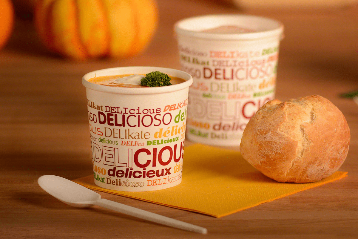 Rausch Verpackung. Suppen to go Becher, geformt wie ein Getränke to go Becher. Beide in Weiß gehalten mit buntem Schriftzug- Aufdruck. Gefüllt sind sie mit einer Suppe und grünem Gemüsedekor. Daneben ist ein helles Weizenbrötchen gelegt.