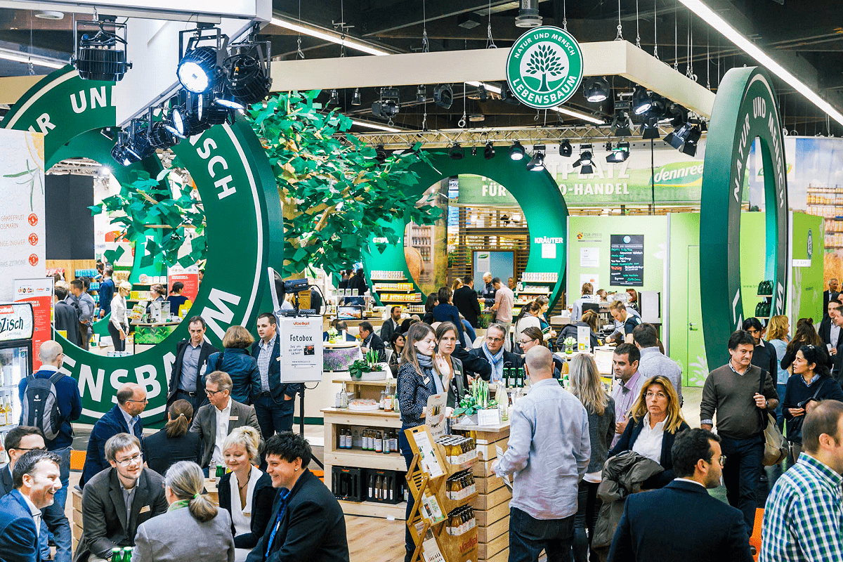 Auf dem Bild sind Aussteller der Leitmesse für Bio-Lebensmittel, der Biofach, zu sehen. Große grüne Runde Kreise dekorieren den Raum.