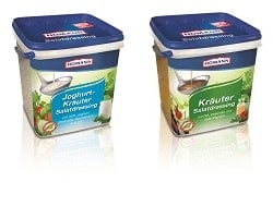 Homann Salatdressing- Verpackungen von den Sorten: Joghurt Kräuter und Kräuter Dressing. Beide stehen nebeneinander auf hellem Hintergrund und Spiegln sich vorne im Bild