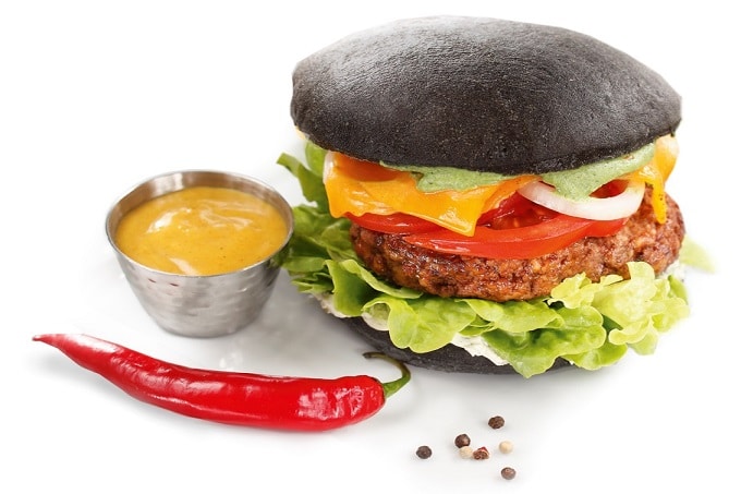 Ein Rezept für einen Black Burger Classic von Edna mit schwarzem Burger Brot, Bulette, Zwiebeln, Tomaten, Salat, Käse und einer Chilischote