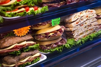 Auf dem Bild sind verschiedene Sandwicharten zu erkennen, die in einem Regal liegen. Sie sind mithilfe von Schildern mit Namen und Preisen gekennzeichnet.