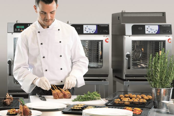 Auf dem Bild ist ein Koch zu erkennen, welcher Snackgerichte auf Tellern anrichtet. Im Hintergrund sind 3 verschiedene Modelle des Convotherm minis des Herstellers Welbilt zu sehen.