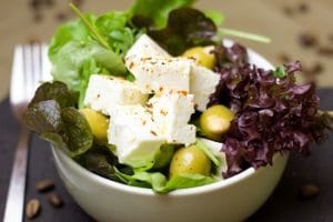 Ein Salat in einer Schüssel gefüllt mit Schafskäse, Oliven und Salatblättern. Neben der Schüssel liegt eine Gabel.