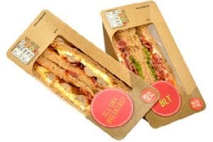 Zwei Sandwiches in einer typischen dreieckigen Sandwichverpackung. Ein Sandwich ist mit Speck, Salat und Tomaten belegt, das andere mit Speck und Ei