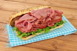 Ein Sandwich mit Salat und Scheibenweise Pastrami, liegend auf einer Servierte auf einem Holztisch.