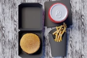 Ein Burger in einem schwarzen Pappkarton, Pommes in einer Pappschachtel und ein Getränk auf schwarzer Pappe
