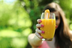 Eine Frau die einen Glas Orangensaft in der Hand hält. Am Rand des Glases hängt eine Orangenscheibe.