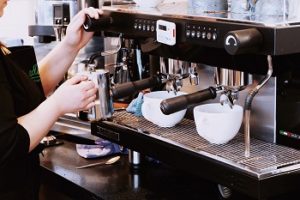 Eine Frau die eine Kaffeemaschine bedient. An der Kaffeemaschine stehen zwei Kaffeetassen.