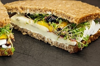 Schwarzbrot mit Camembert, honig senf, sprossen, salat und preiselbeeren belegt. gezeigt an der Schnittkante vegetarisch und vegan