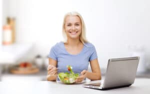 Frau isst Salat vor dem Laptop