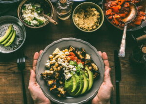 Female hands holding with healthy vegetarian bowl with various grilled vegetables, avocado and chickpea hummus on rustic background, top view. Clean food and dieting nutrition concept / snackconnection