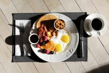 Frühstück mit Spiegelei, Bohnen und Bacon und Kaffee auf einem Tischset / snackconnection