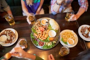 leisure, food, drinks, people and holidays concept - friends eating snack and drinking beer at bar or pub