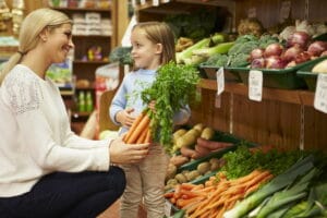 Frau und Kind im Supermarkt am Gemüseregal, Kind hält Karottnbündel / snackconnection