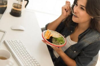 Young woman having breakfast on the computer desk / snackconnection