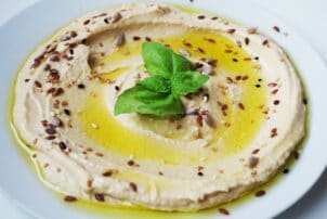 Hummus in einer Schüssel mit Olivenöl, sesam und Minze garniert / snackconnection